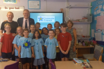 Photo shows John with Headteacher, Michael Wade, and pupils and staff at the school.